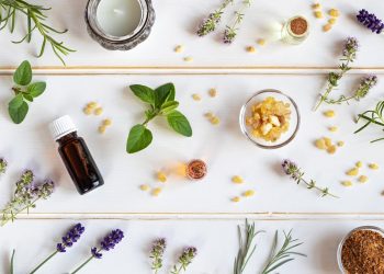 su uno sfondo bianco: una boccia di oli essenziali con lavanda, menta, rosmarino sparso sul tavolo