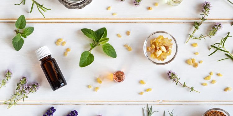 su uno sfondo bianco: una boccia di oli essenziali con lavanda, menta, rosmarino sparso sul tavolo