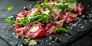 su tagliere di marmo nero primo piano di un carpaccio di manzo con rucola e Parmigiano