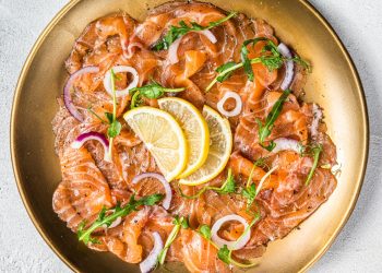 su sfondo grigio piatto dorato con carpaccio di salmone