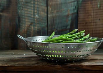 su sfondo di legno uno scolapasta d'acciaio con asparagi verdi per spiegare come pulire gli asparagi