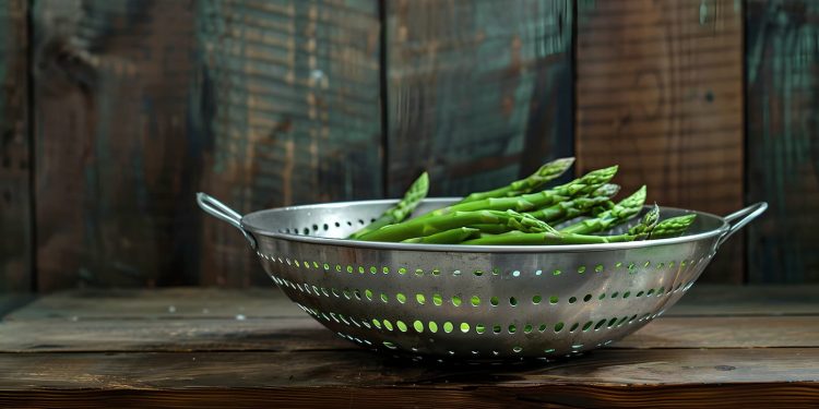 su sfondo di legno uno scolapasta d'acciaio con asparagi verdi per spiegare come pulire gli asparagi