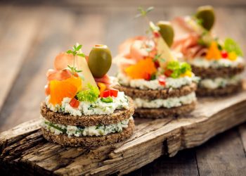 su un tagliere di legno 3 finger food con pane integrale formaggio, salmone e olive