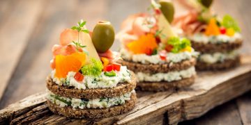 su un tagliere di legno 3 finger food con pane integrale formaggio, salmone e olive