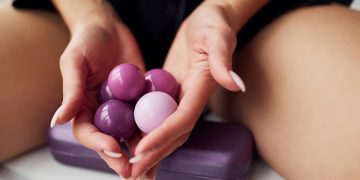 una donna seduta tiene in mano delle palline vaginali rosa e ha un dispositivo elettrico viola accanto a lei
