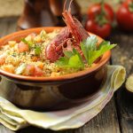 pentola di coccio con cous cous di pesce su tavolo di legno