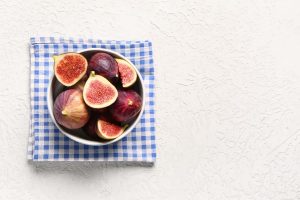 Iscriviti subito alla dieta Melarossa e scarica l'app 10 Fichi freschi interi e tagliati in una ciotola bianca sopra un tovagliolo a quadri azzurro e bianco, su fondo chiaro.