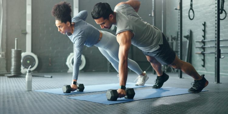 un coppia in palestra con fisico perfetto in posizione di plank che si allena con i pesi