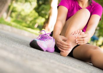 Una giovane donna seduta per terra che si massaggia un piede con un crampo da potassio basso