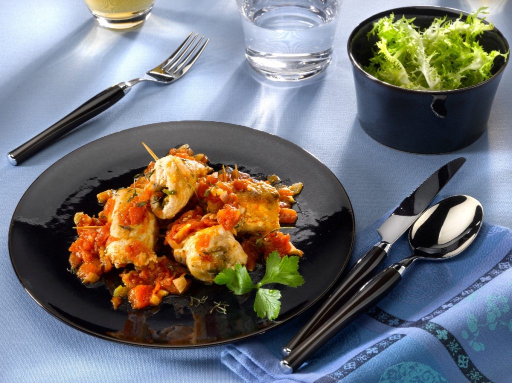 Involtini di pesce spada: un secondo piatto estivo 2 su tavolo apparecchiato, piatto nero con involtini di pesce spada e un bicchiere di acqua e di vino bianco e in una ciotola insalata verde.