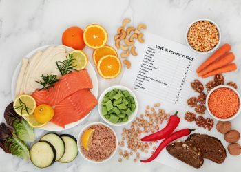 su piano di marmo, foglio con indice glicemico alimenti e attorno cibo come lenticchie rosse, salmone, peperone rosso, carote e frutta secca