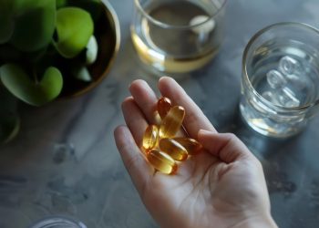 Mano di una donna con integratori per stanchezza fisica e mentale. In secondo piano un bicchiere di acqua e limoni