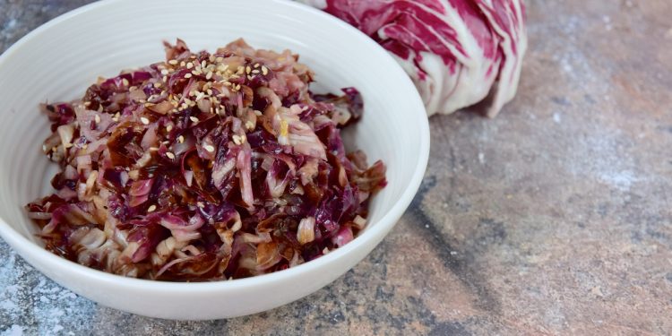 su tavolo di marmo, radicchio in padella in una ciotola bianca con semi di sesamo e dietro un radicchio