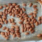 primo piano di mani che tengono una teglia da forno con carta da forno e mandorle tostate