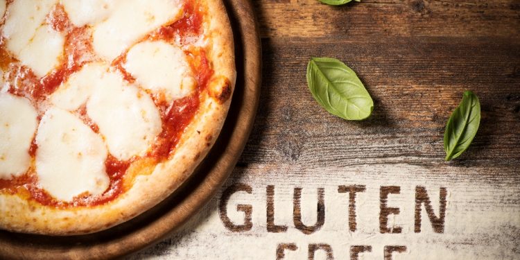 su tavolo di legno: farina sparsa e basilico con a sinistra metà di una pizza senza glutine con a destra la scritta gluten free