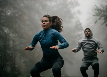 In un bosco con la nebbia una coppia che eseguono salti durante un workout HIIT