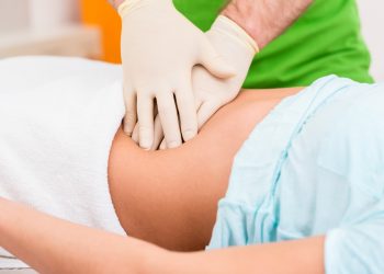 donna distesa su lettino che sta per eseguire una idrocolonterapia, mani di un medico che gli esegue un massaggio del colon