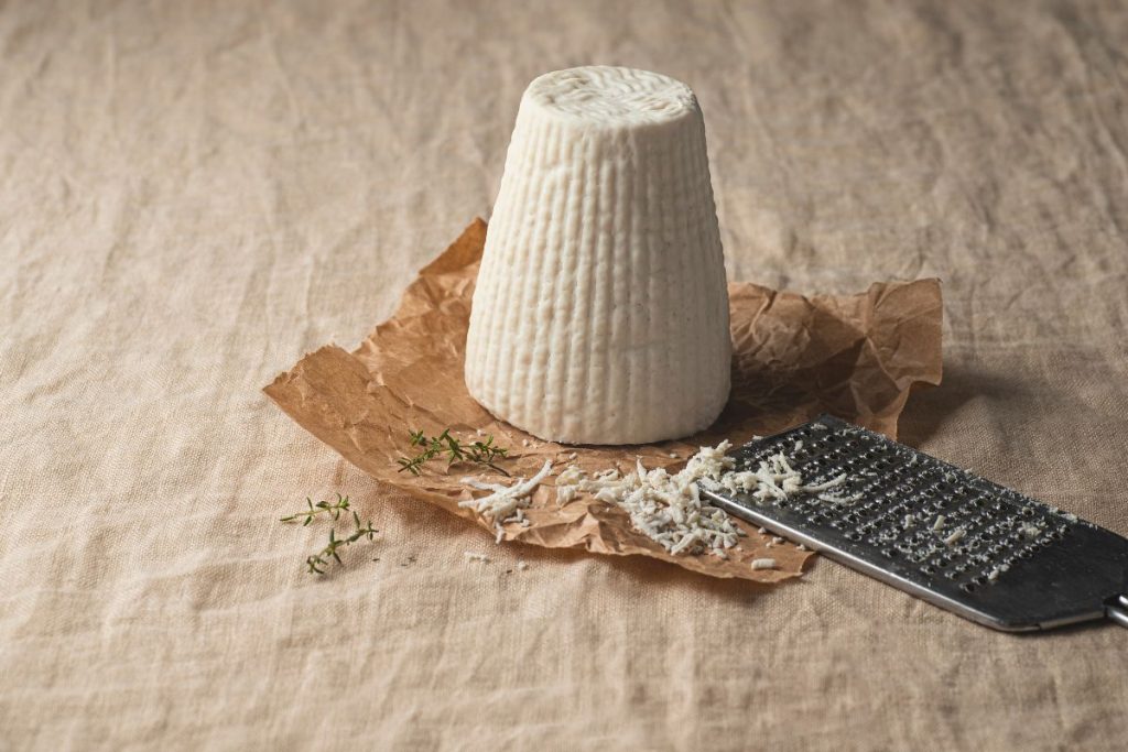 una forma di ricotta salata con accanto una grattugia