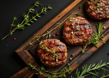 Su tavolo di legno, tagliere con 3 hamburger di carne , pepe nero, erbe aromatiche