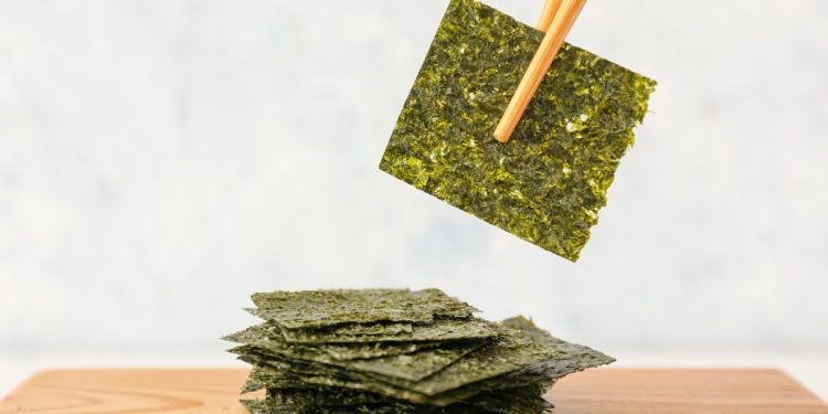 su tavolo tagliere di legno con fogli di alga Nori e un foglio in alto con le bacchette cinesi