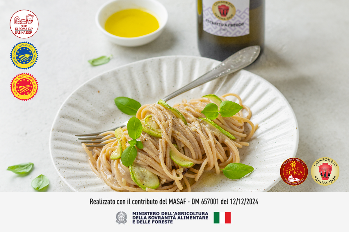 Primo piano di un piatto di spaghetti alla Nerano con basilico e una forchetta, dietro una bottiglia di olio EVO e sulla destra una ciotola con olio. In alto a sinistra loghi dell' olio e anche in basso a destra