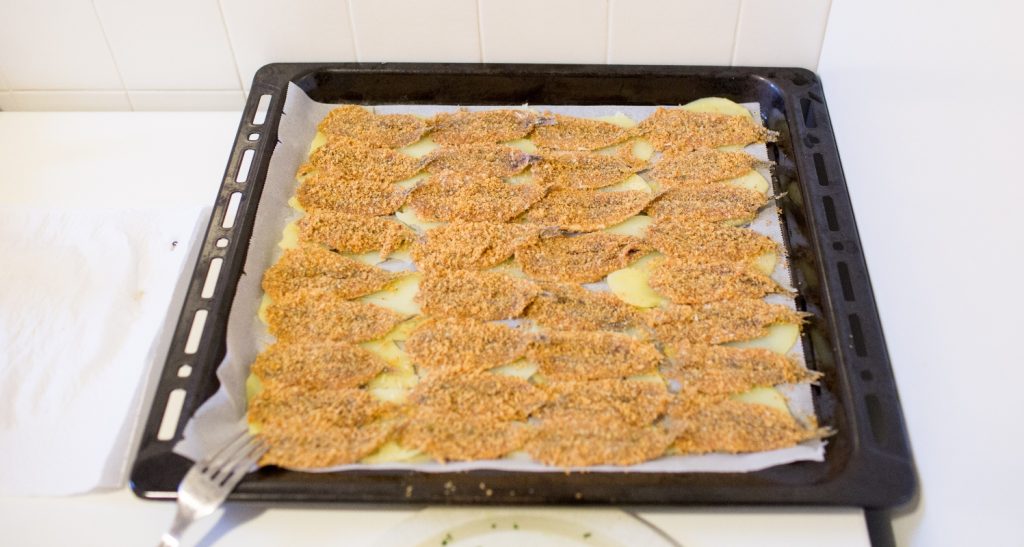 Alici al forno: un ricetta croccante e saporita 4 su sfondo bianco, teglia con alici al forno e sotto patate tagliate a fette sottili