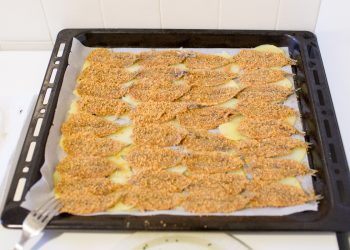 su sfondo bianco, teglia con alici al forno e sotto patate tagliate a fette sottili