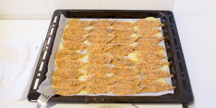 su sfondo bianco, teglia con alici al forno e sotto patate tagliate a fette sottili