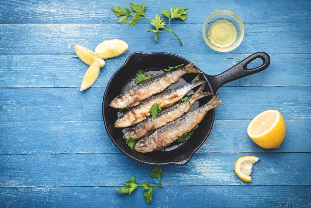 ricette con alici: su tavolo di legno azzurro, alici in padella con prezzemolo e fette di limone