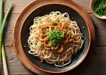 su tavolo di legno, piatto con noodles e cipollotti tagliati , sualla destra un cipollotto e a destra ciottola con cipollotto tagliato