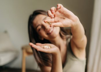 donna in soggiorno sorridente che tiene in mano integratori di fibre e fa vedere la pillola nell'altra mano