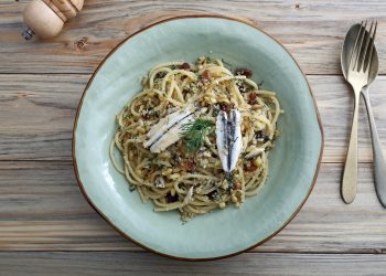 su tavolo di legno piatto fondo azzurro con pasta con le alici; sulla destra cucchiaio e forchetta