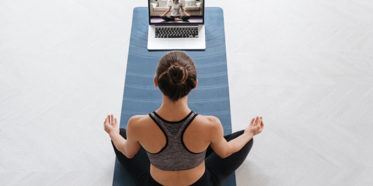 per un articolo su tappetini yoga, una donna seduta su un tappeto nella posizione semplice davanti ad un computer con una lezione di Yoga