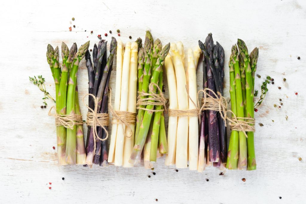 su sfondo bianco mazzi di asparagi bianchi, verdi e viola per illustrare come cucinare gli asparagi