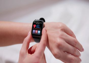 sul braccio di una donna un contapassi con uno schermo che mostra varie funzionalità su uno sfondo chiaro