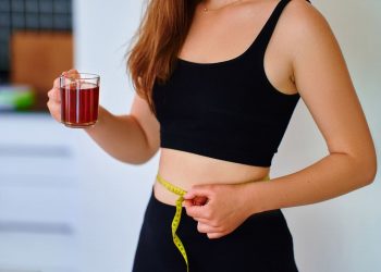 integratori per pancia gonfia: una giovane donna che beve una tisana e misura il giro vita con un centimetro