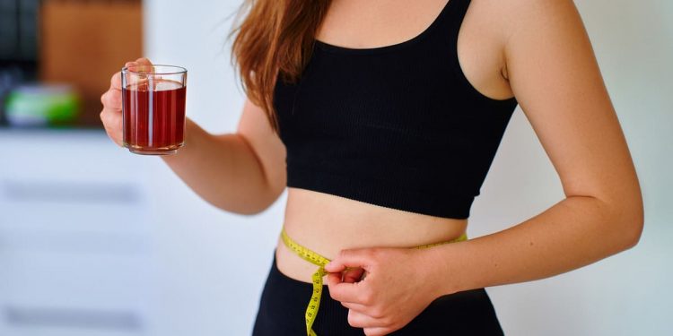 integratori per pancia gonfia: una giovane donna che beve una tisana e misura il giro vita con un centimetro
