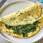 ricette con frittata: in primo piano, un piatto bianco con una frittata di albumi con la verdura dentro. Accanto un coltello azzurro