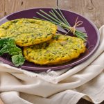 ricette con frittata: su tavolo di legno, canovaccio beige con sopra un piatto viola con frittata di spinaci, erba cipolline e una foglia di spinaci freschi