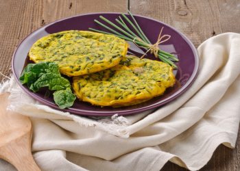 ricette con frittata: su tavolo di legno, canovaccio beige con sopra un piatto viola con frittata di spinaci, erba cipolline e una foglia di spinaci freschi