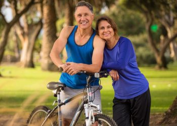 un uomo e una donna sulla cinquantina appoggiati a una bicicletta in tuta sportiva perché è possibile rimettersi in forma a 50 anni