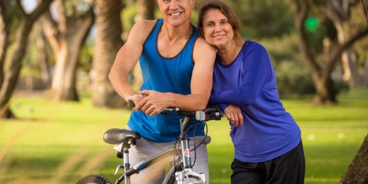 un uomo e una donna sulla cinquantina appoggiati a una bicicletta in tuta sportiva perché è possibile rimettersi in forma a 50 anni