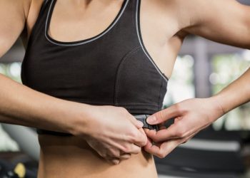 mezzo busto di una donna con un reggiseno sportivo nero, sullo sfondo attrezzi della palestra