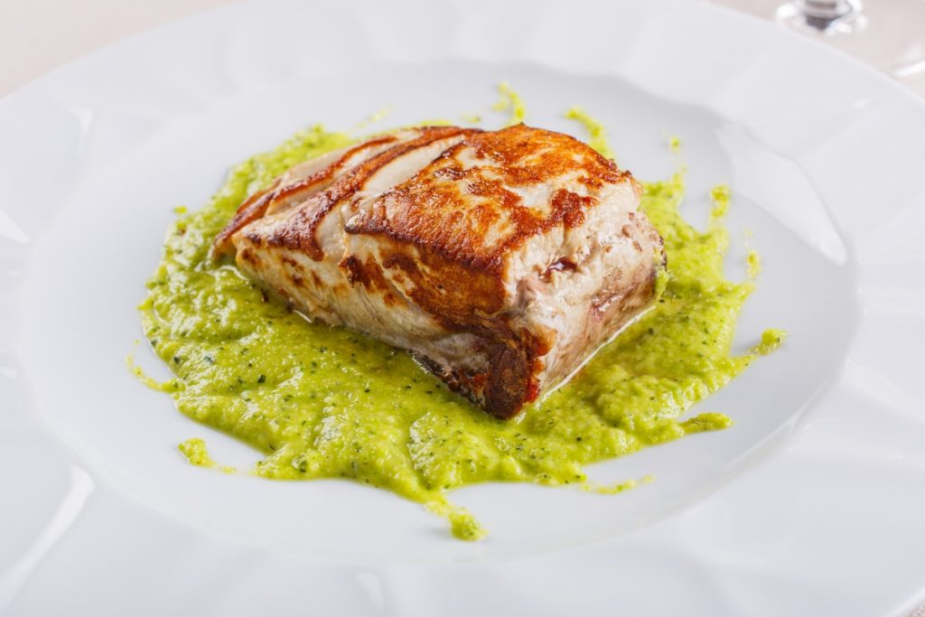 Ricciola al forno: un secondo piatto di pesce sano e gustoso 1 primo piano di un piatto con la ricciola al forno su un letto di crema di zucchine alla scapece servito in un ristorante elegante