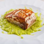 primo piano di un piatto con la ricciola al forno su un letto di crema di zucchine alla scapece servito in un ristorante elegante