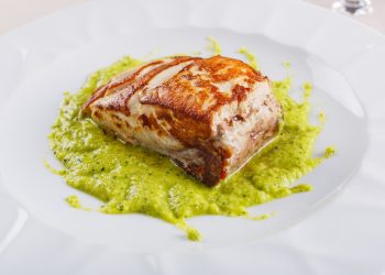 primo piano di un piatto con la ricciola al forno su un letto di crema di zucchine alla scapece servito in un ristorante elegante