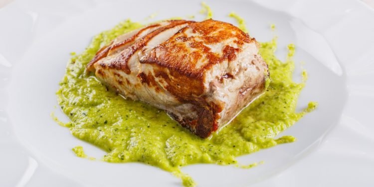 primo piano di un piatto con la ricciola al forno su un letto di crema di zucchine alla scapece servito in un ristorante elegante