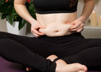 skinny fat: una donna seduta a gambe incrociate che mostra un po' di grasso addominale