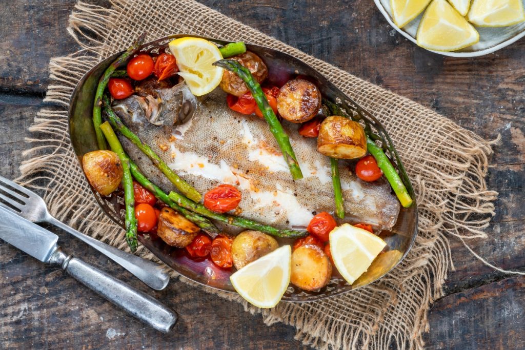 su tavolo di legno sotto tavolo stile bohémien con un piatto con sogliola al forno, patate, asparagi, pomodorini con alcune fette di limoni . Sulla sinistra forchetta e coltello