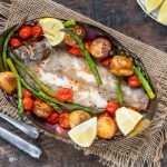 su tavolo di legno sotto tavolo stile bohémien con un piatto con sogliola al forno, patate, asparagi, pomodorini con alcune fette di limoni . Sulla sinistra forchetta e coltello